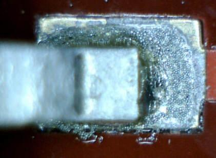 a close-up view of a small electronic component, possibly a white connector or switch, positioned in the center on a red background, resembling a wooden surface.