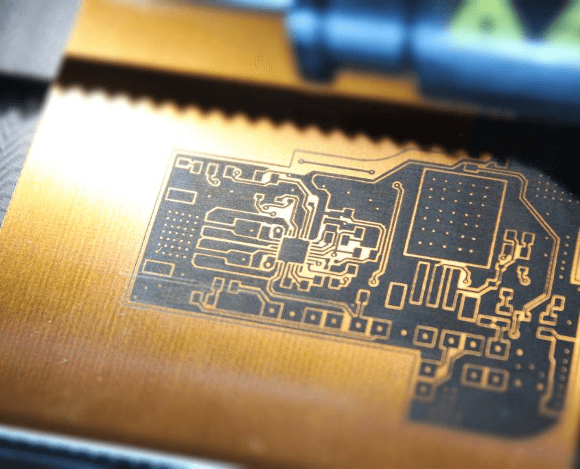 Close-up on gold circuit board coated with varnish, connected to other components through black lines.