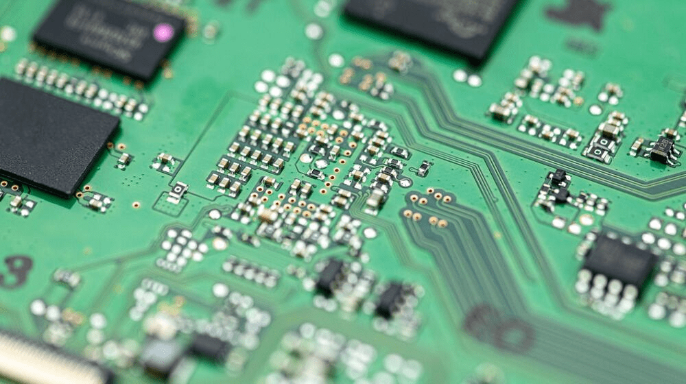Close-up view of a green circuit board featuring a wide dispersion of electrical components, including prominent chips. The image captures a technical atmosphere, highlighting the intricate nature of the electronics.