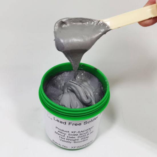 Hand holding a spatula for lifting white paste from an open green container