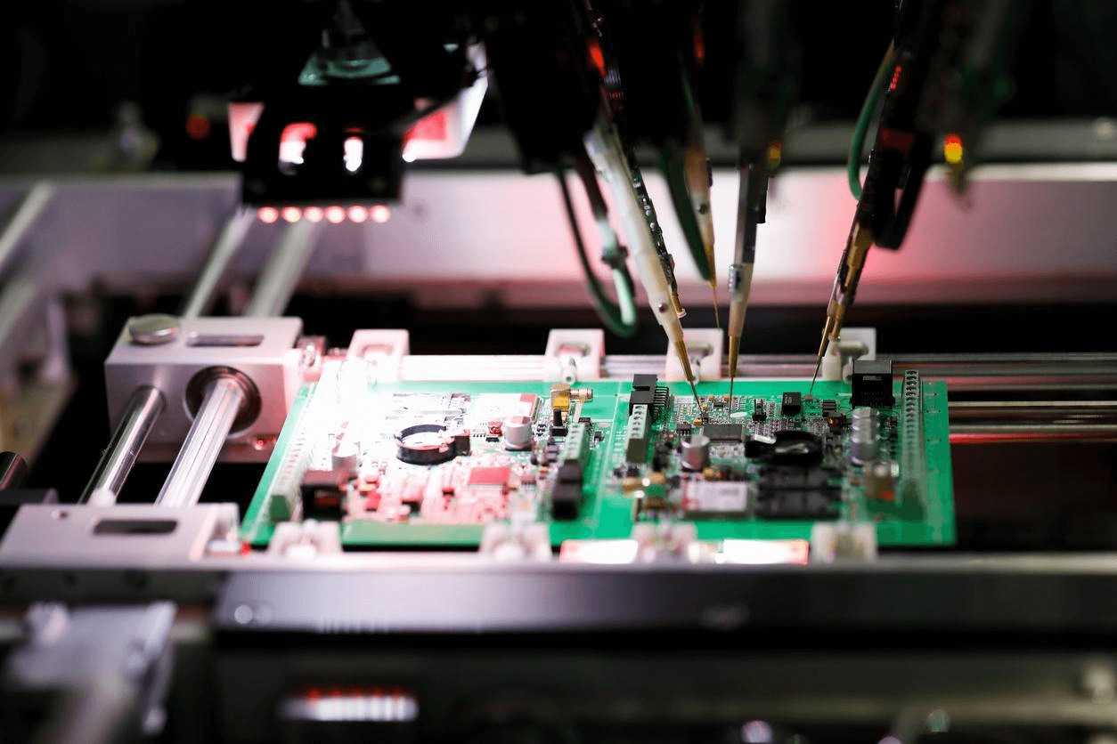 Automated assembly process in a factory. Robotic arm precisely placing electronic components on a green PCB. Blurred background, focusing on the robot arm and PCB. Dark atmosphere with red lighting, creating an industrial ambiance. Two visible red components on the PCB, additional component colors unclear.